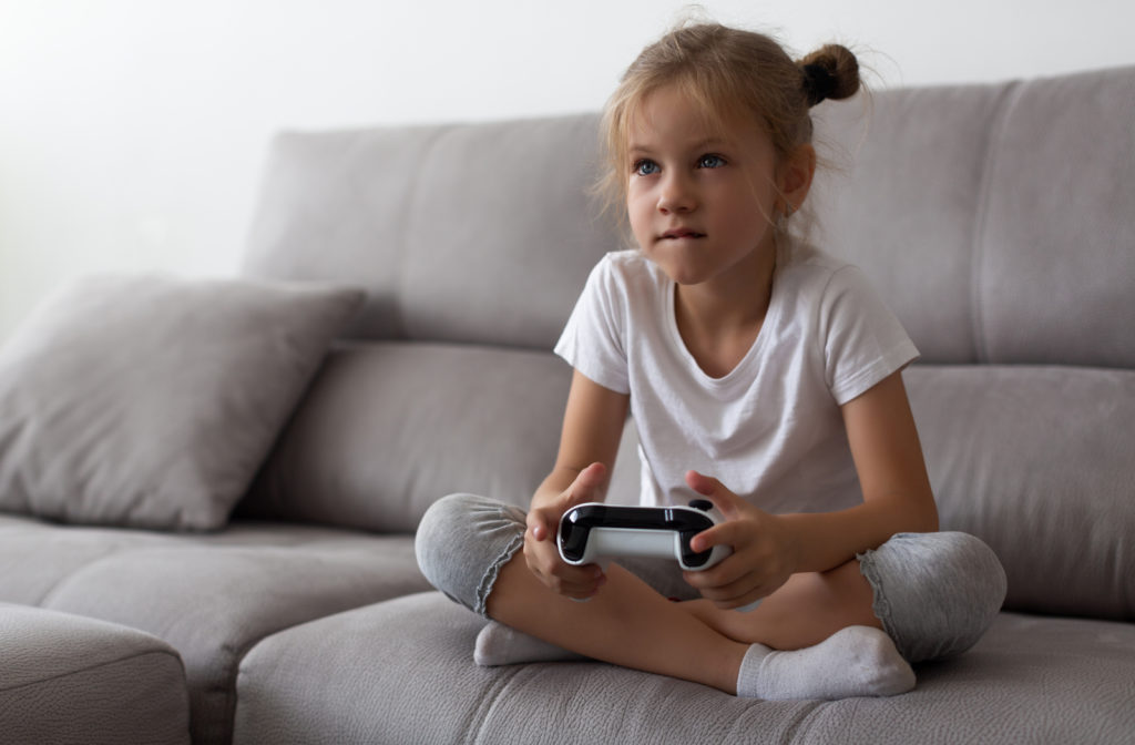 Young girl sitting on couch playing video games and not going outdoors which may be the cause of why her myopia is getting worse.