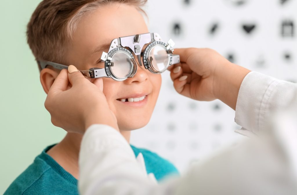 A young boy wearing a pair of trial frames as the female optometrist adjusts them.