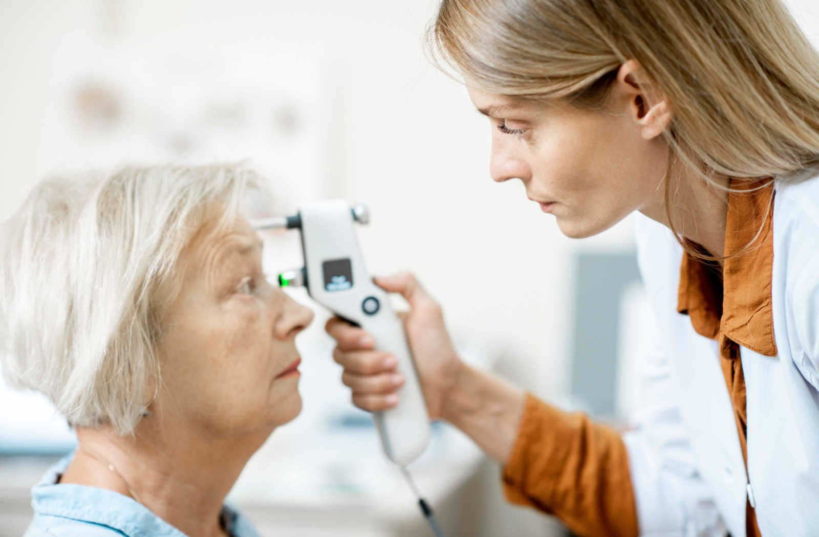 Female optometrist measuring the eye pressure of a senior woman with a modern tonometer to screen for glaucoma.