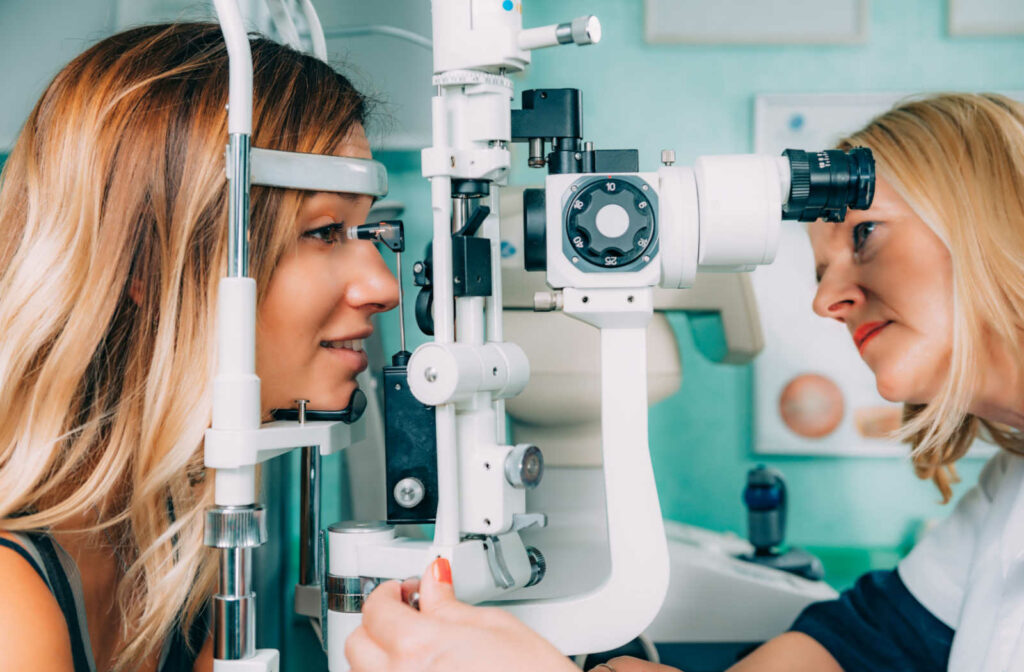 An optometrist is preparing a young female patient for applanation tonometry, the patient's chin is resting on a chin rest and looking through a slit lamp.