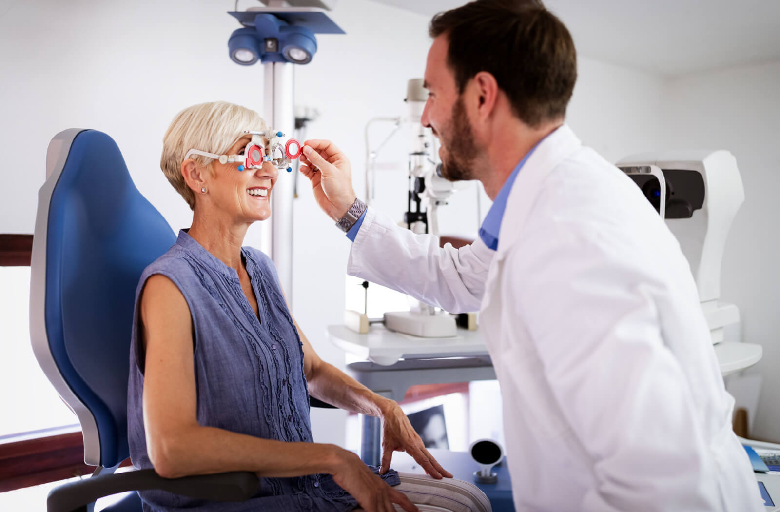 A senior woman and her male optometrist performing an eye exam using a medical device to detect eye problems.