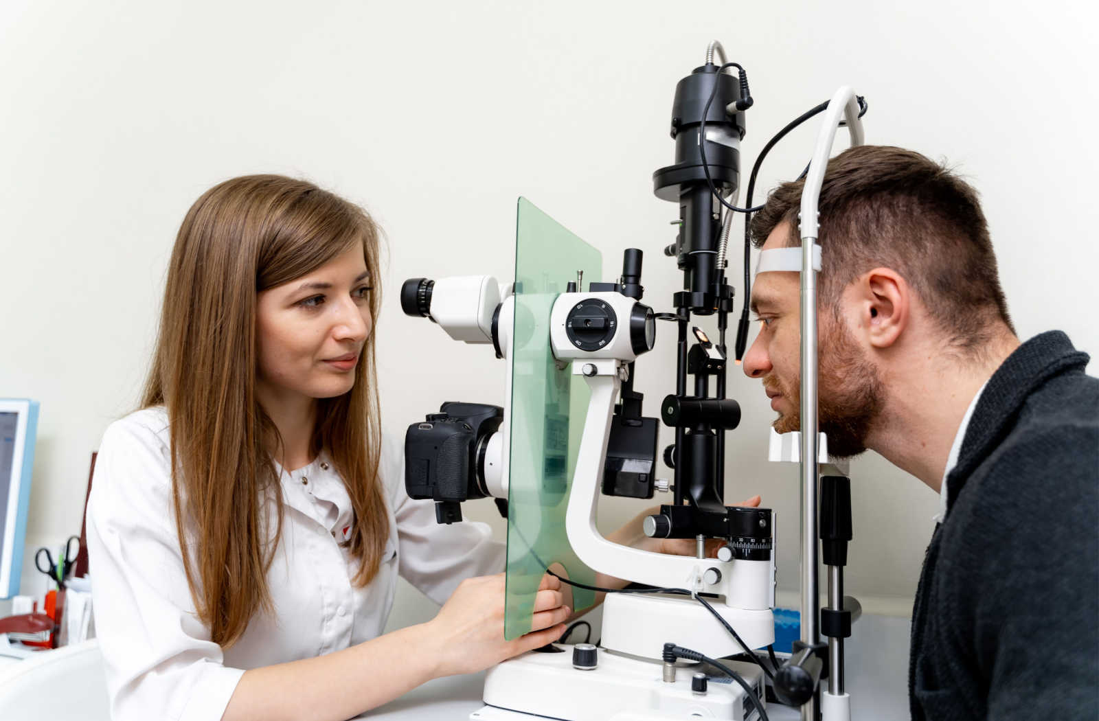 A female optometrist examines the eyes of a man using a medical device to detect potential eye problems.