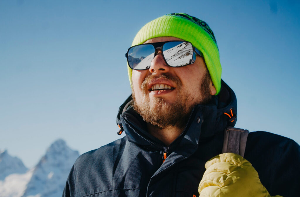 Close-up of a man standing on a mountaintop wearing reflective sunglasses and winter gear.