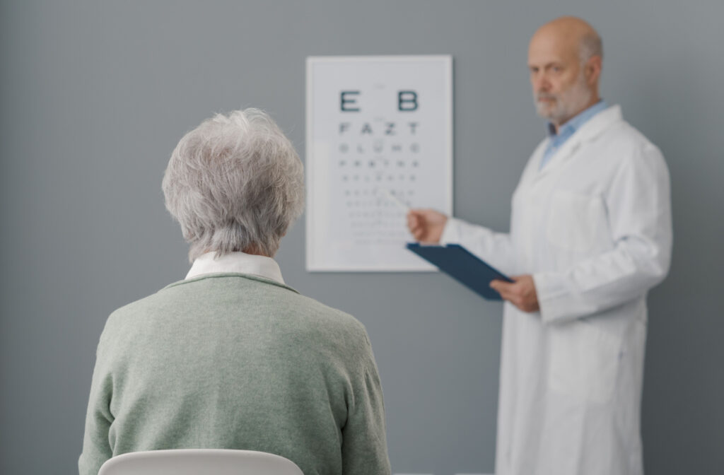 View from behind a senior patient's head as they face a snellen chart on the wall and their optometrist points to a letter.