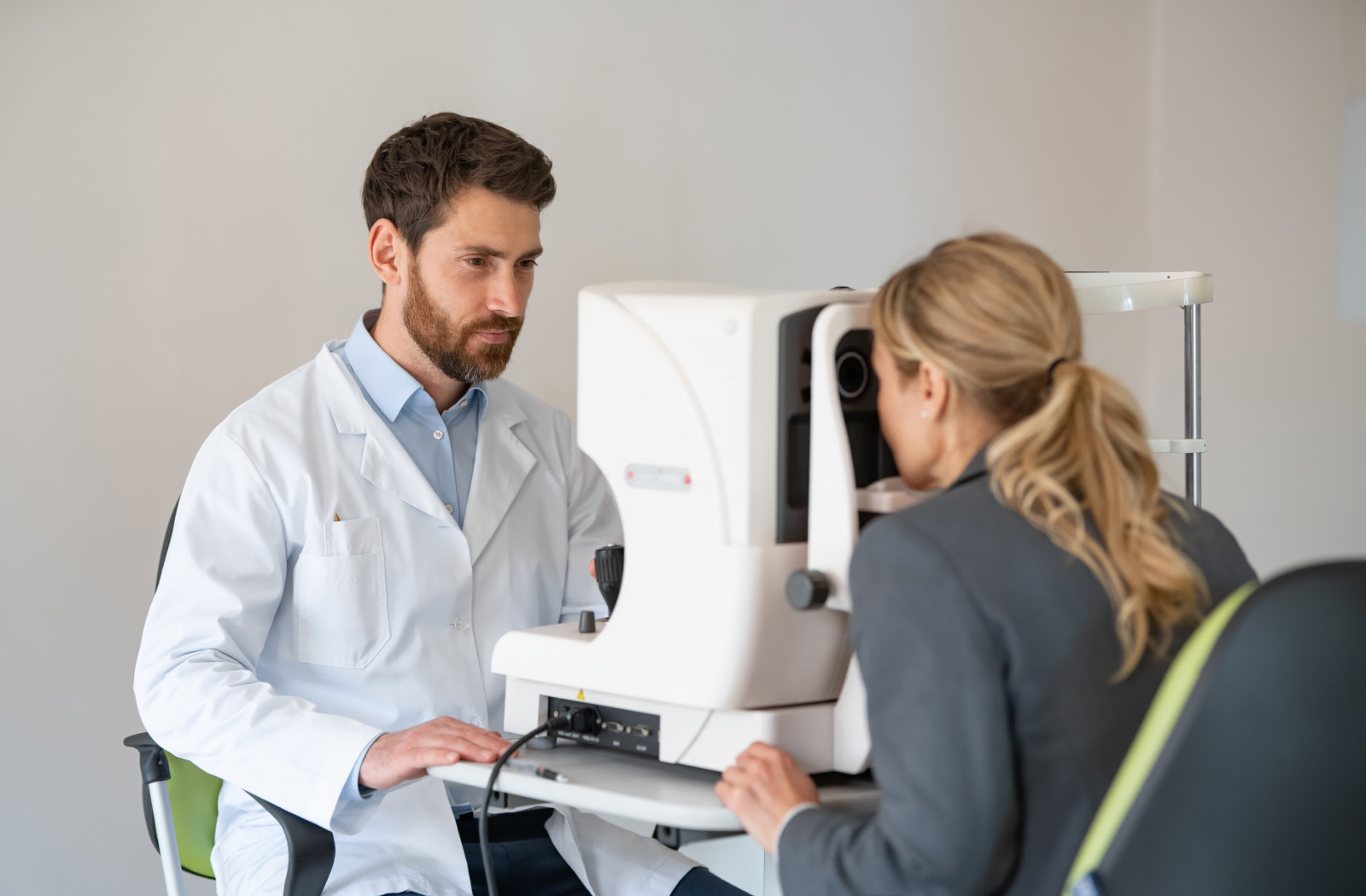 A male optometrist using a medical device to examine the eyes of a female patient.