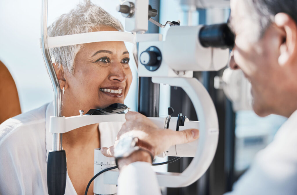 A senior woman smiling and looking into a piece of optometry equipment as his optometrist performs an eye exam.