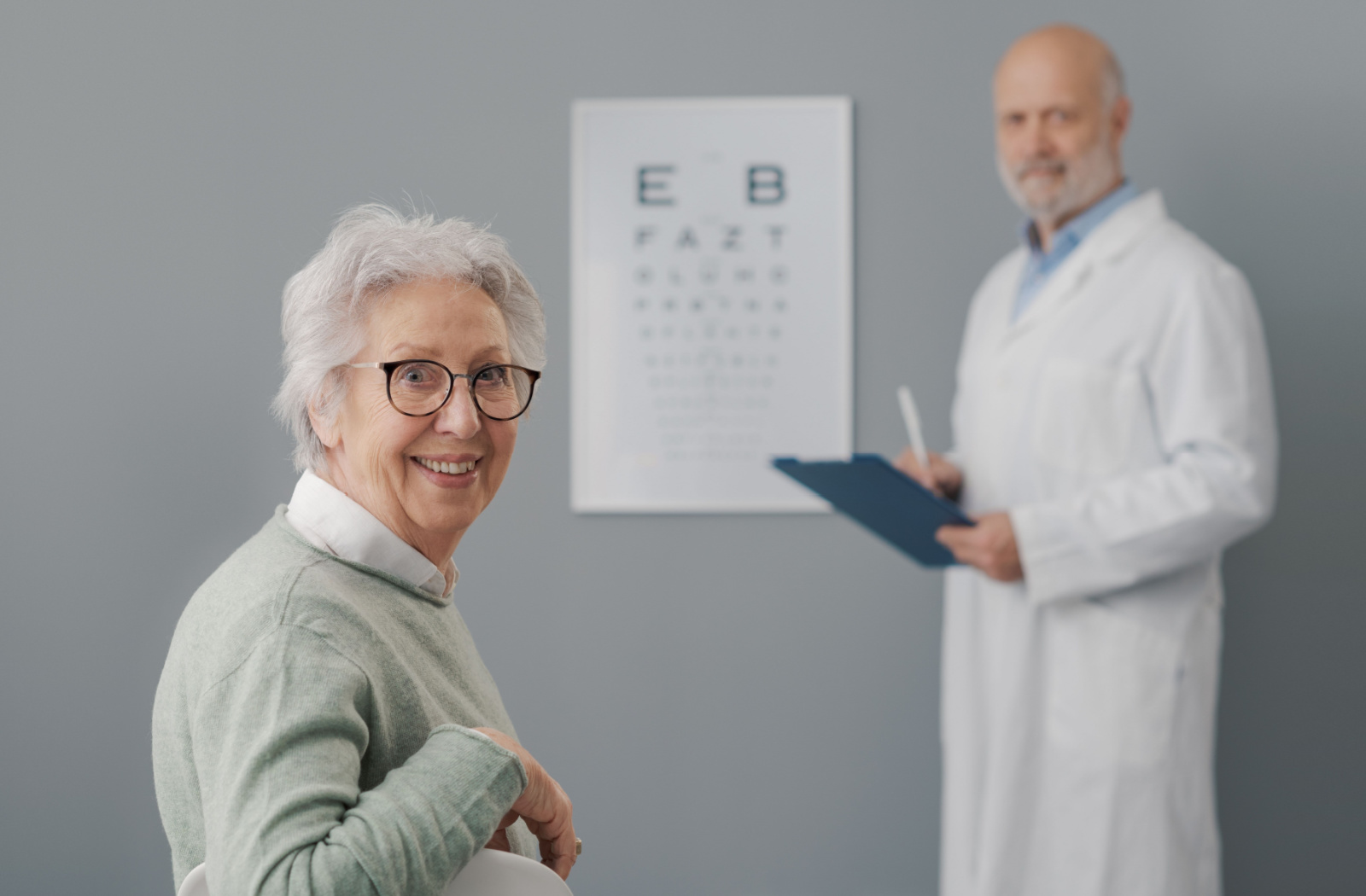 An optometrist conducting an eye exam on a senior woman with glasses.
