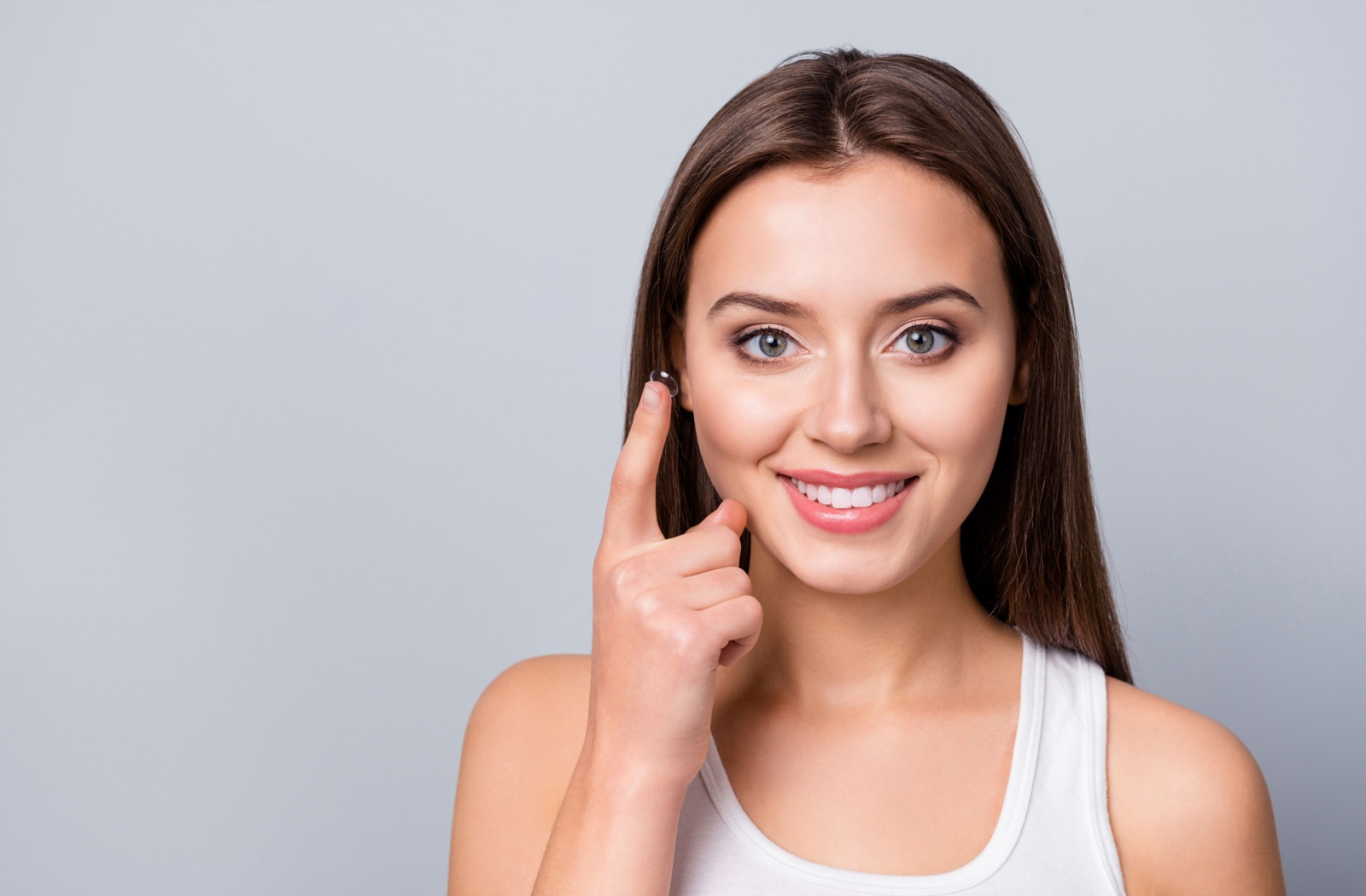 young woman smiling and holding contact on right pointer finger.
