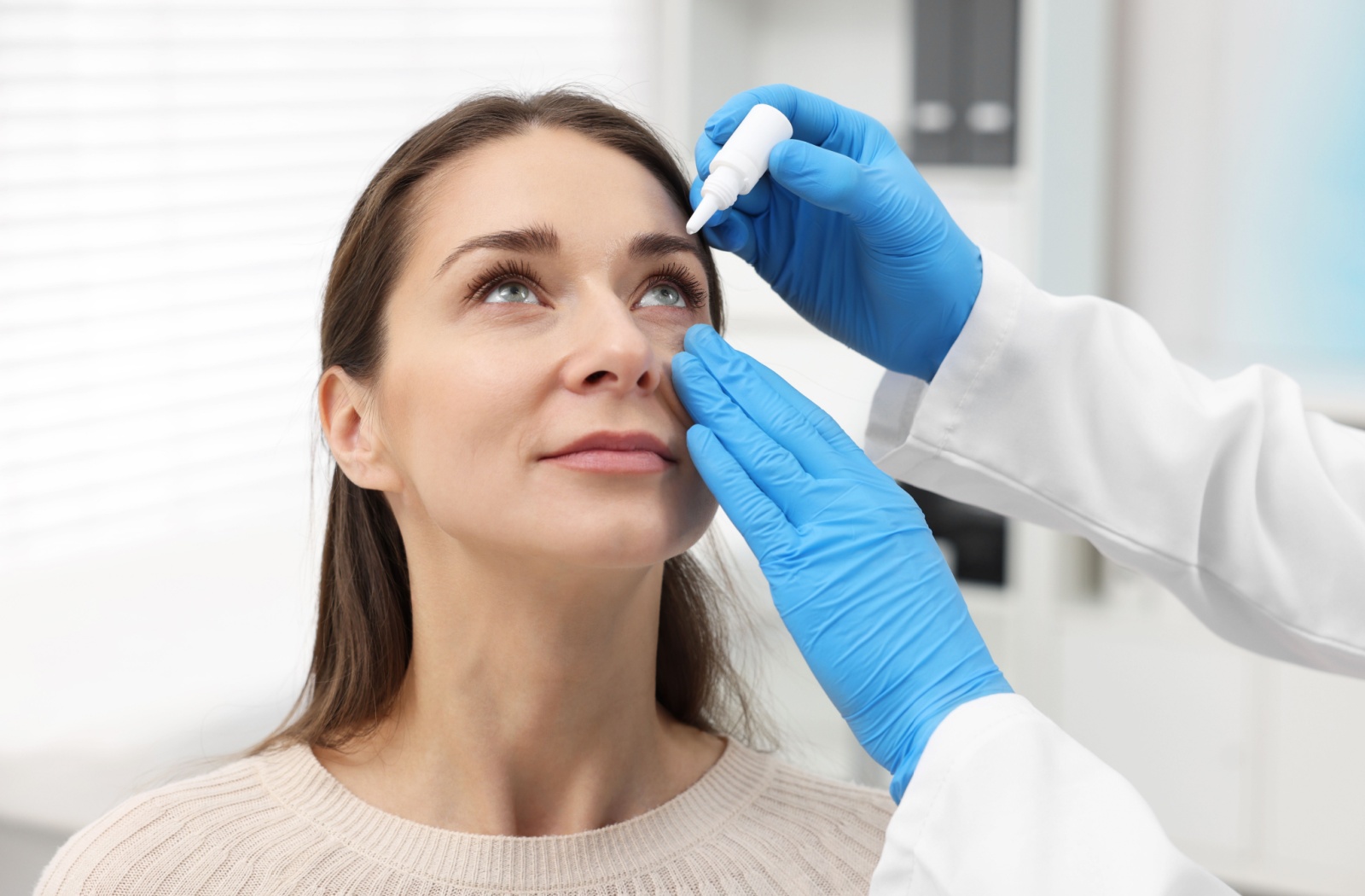 Optometrist administering prescription eye drops to a female patient.