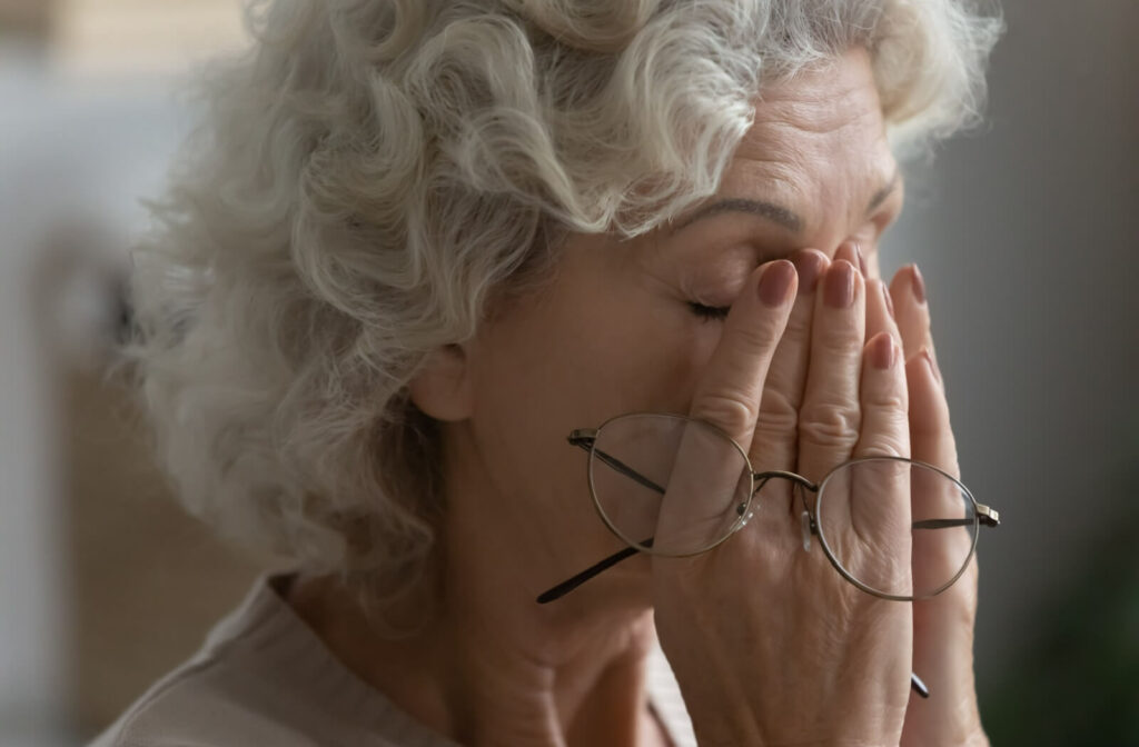 An older adult rubbing their eyes because of cloudy vision caused by cataracts.