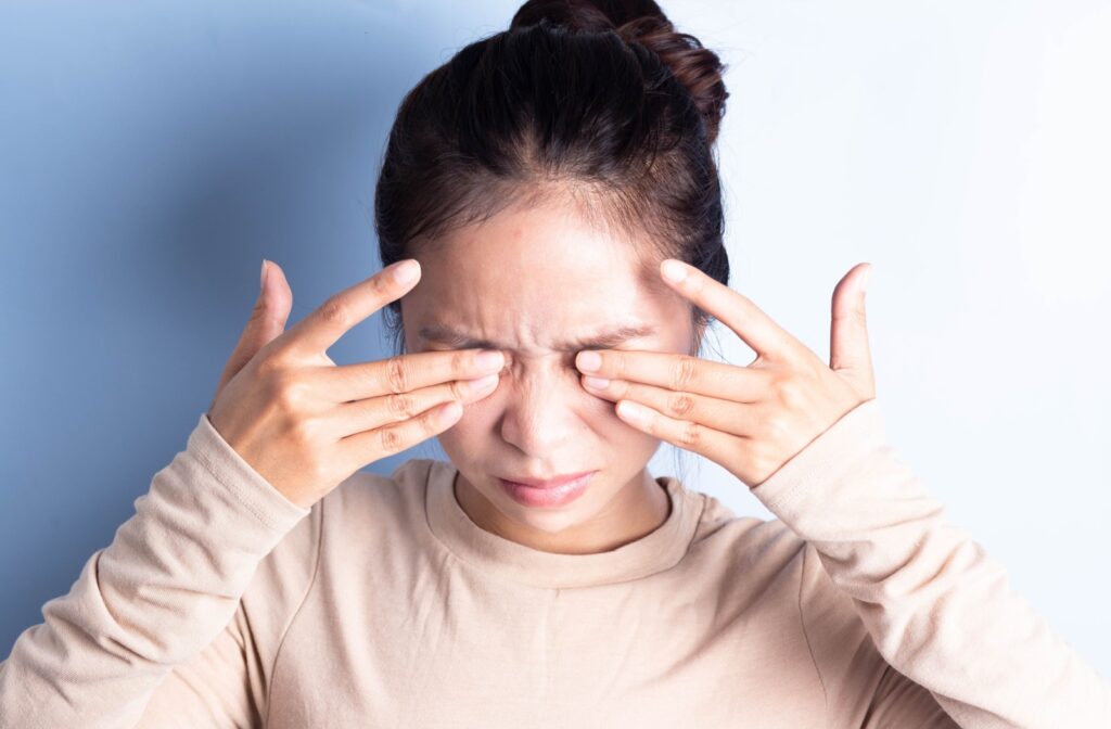 A person covers both their eyes as they wince in pain.