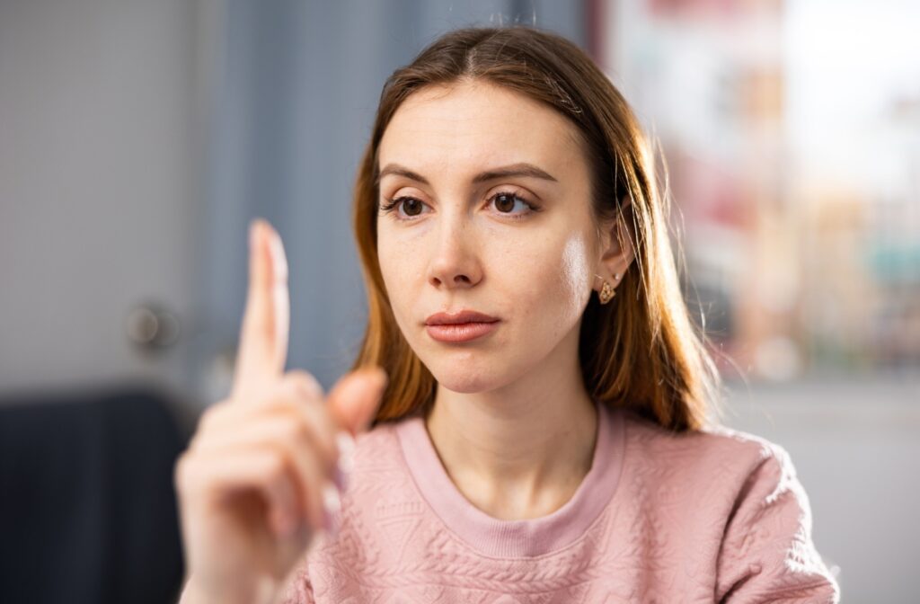 A woman wearing a pink textured sweater holds up her index finger in front of her face while focusing intently on it, likely performing a vision or eye-tracking exercise in a well-lit indoor setting.