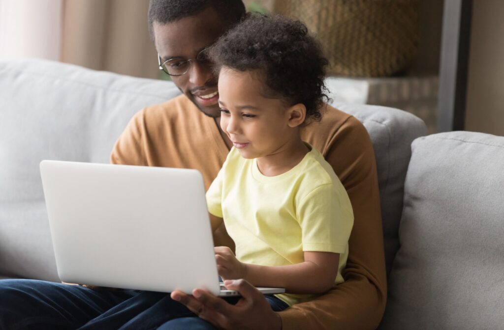 Parent and young child looking at a laptop together seated on a couch.