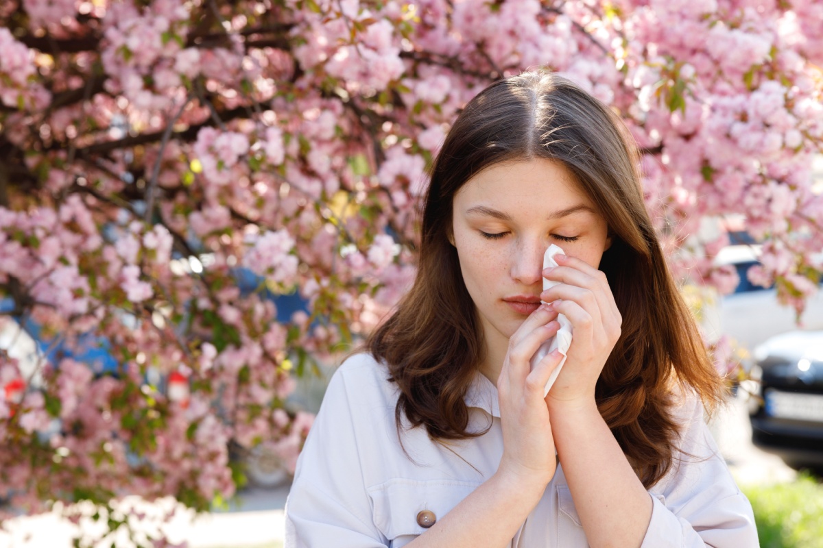 Young woman wiping eyes in front of cherry blossoms.