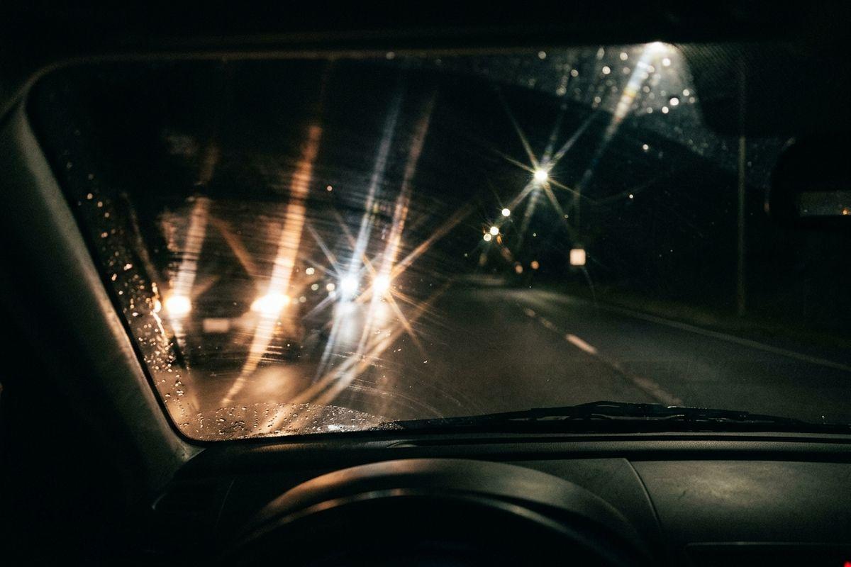 View through a car windshield at night, oncoming headlights glaring and streaking on wet glass.
